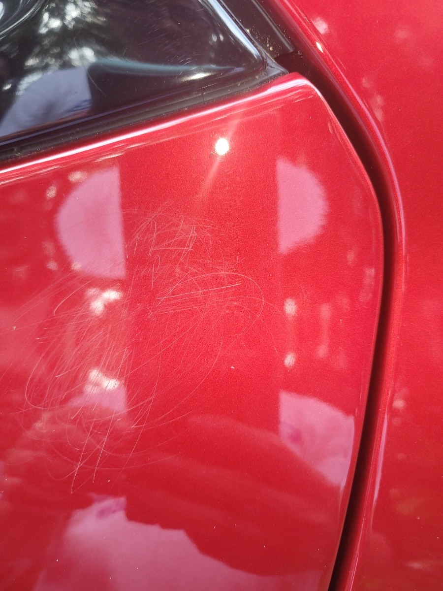 Red car paint covered in scratches and swirl marks before paint correction