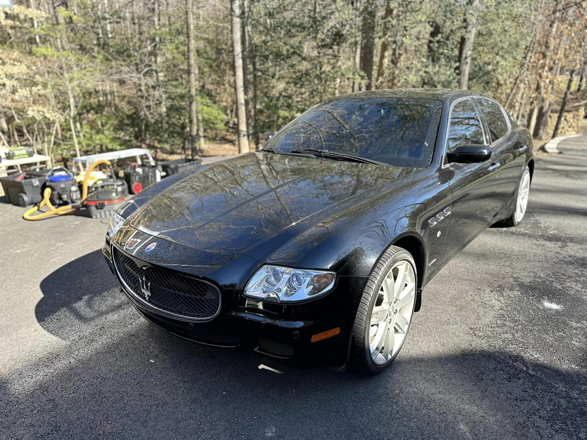 A black Maserati Quattroporte, reflecting trees like a mirror